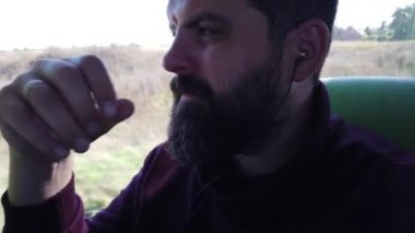İnsan otobüsle seyahat eder. Yolcu otobüsün camından dışarı bakar ve kulaklıkla müzik dinler..