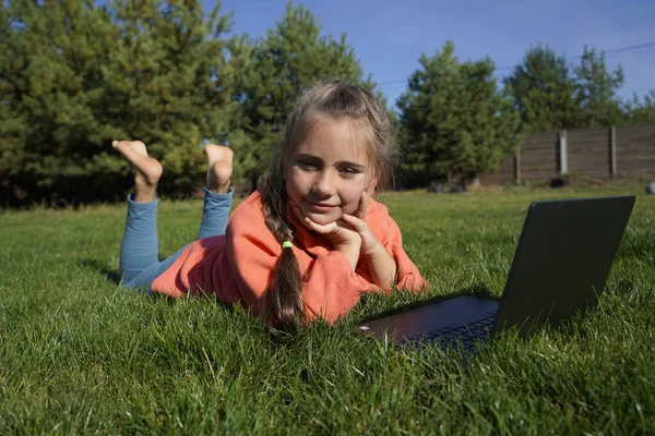 Ein siebenjähriges Mädchen arbeitet auf einem Laptop im grünen Gras. — Stockfoto