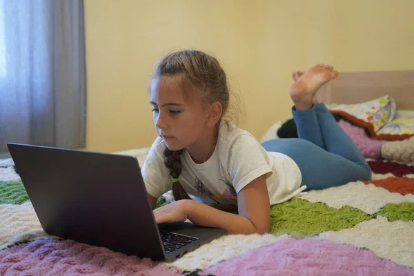 Ein siebenjähriges Mädchen arbeitet an einem Laptop in einem Raum, während es lyin — Stockfoto