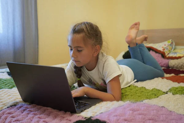 Ein siebenjähriges Mädchen arbeitet an einem Laptop in einem Raum, während es lyin — Stockfoto
