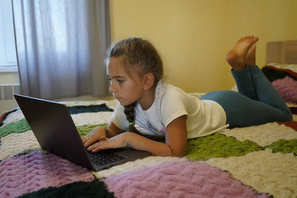 Ein siebenjähriges Mädchen arbeitet an einem Laptop in einem Raum, während es lyin — Stockfoto