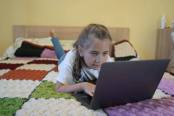 Ein siebenjähriges Mädchen arbeitet an einem Laptop in einem Raum, während es lyin — Stockfoto