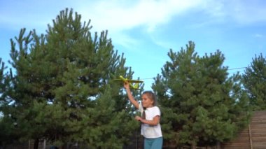 Berlin, Almanya - Ekim 2019: Bir kız, çamların ve mavi gökyüzünün arka planında oyuncak bir uçak fırlatıyor. Doğanın arka planında oyuncak bir uçakla oynayan kız..
