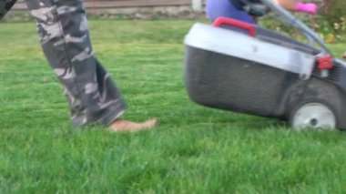 Çim biçme makinesi çimleri biçer. Çimlerin üzerinde çıplak ayaklar.