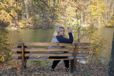 Bir kız gölün arka planında bankta oturuyor.