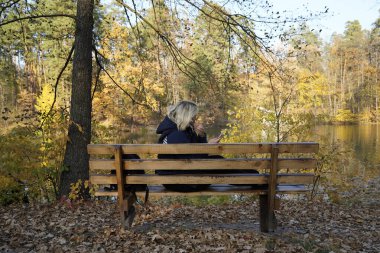 Bankta oturan kız arka planda akıllı telefon kullanıyor.