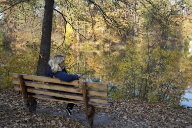 Bir kız gölün arka planında bankta oturuyor.