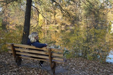 Bir kız gölün arka planında bankta oturuyor.
