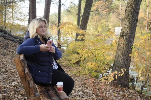 Girl sitting on a bench uses a smartphone on the background of t — Stock Photo, Image