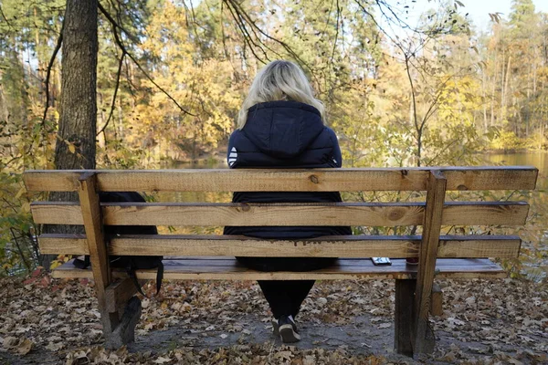 Bir kız gölün arka planında bankta oturuyor.