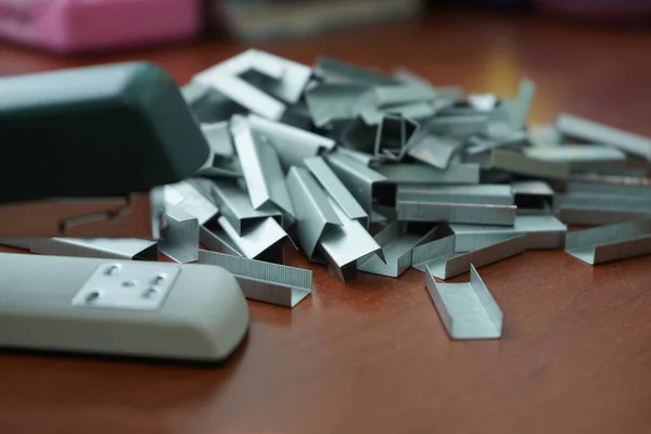 Muitos grampos de um grampeador em uma mesa de madeira. Grampeador com um ramo — Fotografia de Stock