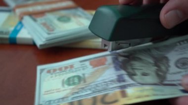 Zımba dolar ve euro banknotlarını demir raptiyelerle tutturuyor. Banknotların arka planında ataç olan zımba. Sahte para.