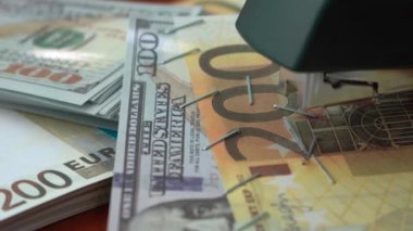 Zımba dolar ve euro banknotlarını demir raptiyelerle tutturuyor. Banknotların arka planında ataç olan zımba. Sahte para.