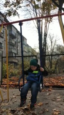 Sonbahar öğleden sonra bir çocuk salıncakta sallanıyor. Çocuk salıncağı. Dikey video.
