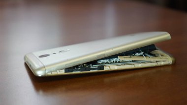 Şişmiş akıllı telefon pili. Bozuk pilli, hasarlı bir akıllı telefon. Ahşap bir arka planda hasarlı telefon.