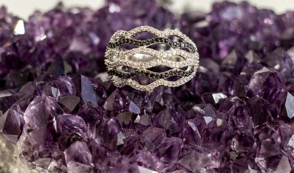 silver ring with small stones of zirconium lies on the purple friends of ametiska