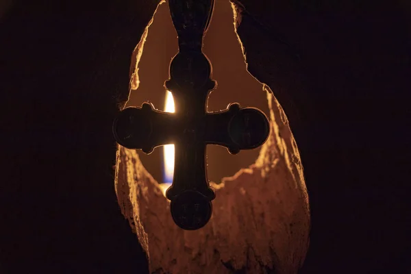 Серебряный Крест Фоне Горящей Свечи Которая Освещает Дыру Стене — стоковое фото