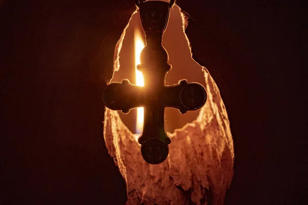 silver cross on the background of a burning candle that gives light from a hole in the wall