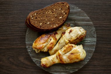 üç kızarmış tavuk bacağı ahşap bir masa üzerinde siyah ekmek bir parça ile cam bir tabak üzerinde yalan