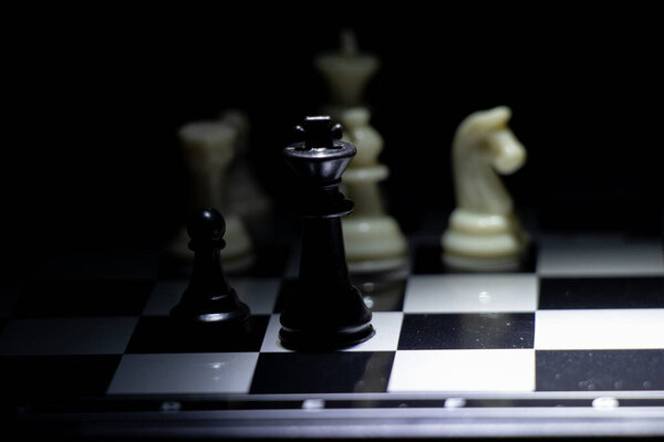 Chess pieces on a chessboard in a dark room illuminated by a lantern