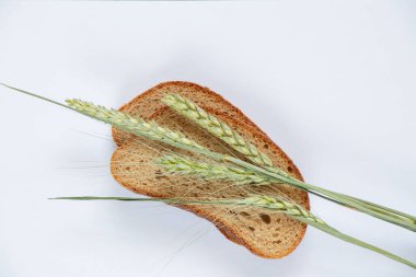 piece of black bread and ears of wheat on a white