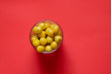 yellow cherries in a glass on a red table