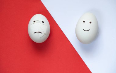 sad and joyful chicken egg on a colored background