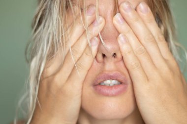 Genç bir kız, izole bir arka planda ellerini yakın plan portresiyle yüzünü kapattı.