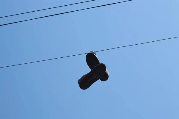 dirty sneakers hang on a wire on a pole against a blue sky