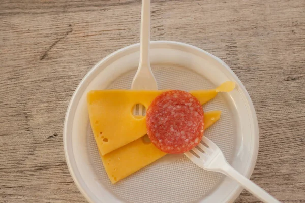 sliced cheese and sausage on a plastic plate with a fork on the table