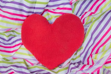 kırmızı kalp şeklinde bir yastık çok renkli bir kumaşın üzerinde yatıyor.