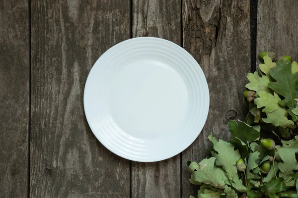 橡木叶和木制桌子上洁白的空盘子 — 图库照片