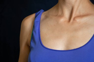 Siyah arka planda mavi tişörtlü bir kızın göğsü.