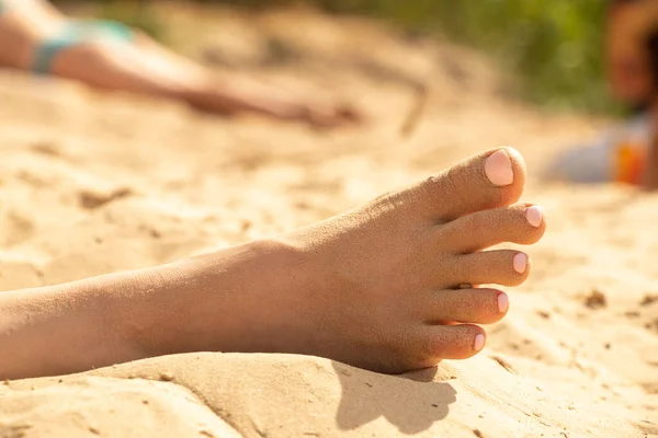 Pierna femenina se encuentra en la arena en el sol en la playa en verano — Foto de Stock