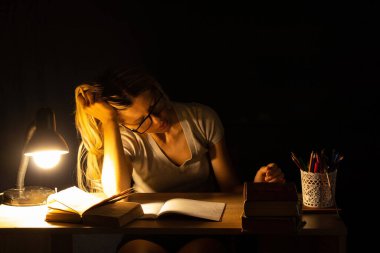 Karanlık bir odada, lambanın ışığında uyuyan, öğrenen, aşırı zorlayan bir kız.