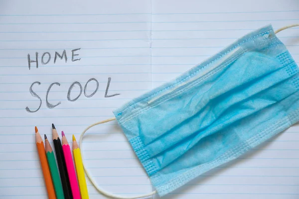 notebook open in a ruler colored pencils and a medical mask on the school desk, home education, quarantine