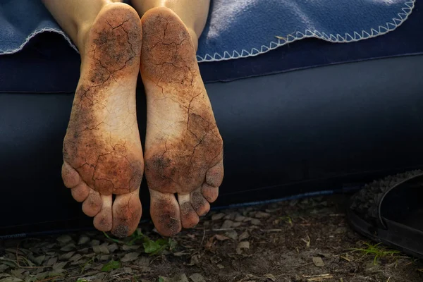 dirty cracked feet of a girl who lies on a mattress in the forest, walking barefoot on the ground