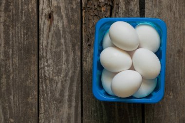 Mutfaktaki ahşap masada mavi bir kutuda beyaz tavuk yumurtaları.