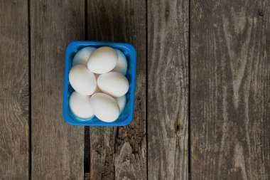 Mutfaktaki ahşap masada mavi bir kutuda beyaz tavuk yumurtaları.