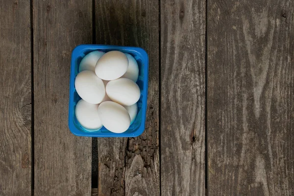Mutfaktaki ahşap masada mavi bir kutuda beyaz tavuk yumurtaları.