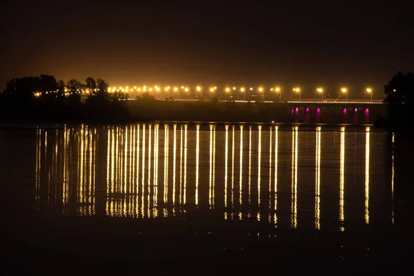 夜晚，在灯柱的灯光下，长距离的暴露在水中，映照在水面上的一座桥 — 图库照片