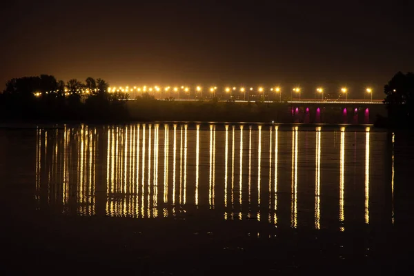 Ponte sobre o rio dnieper à noite nas luzes dos postes de iluminação em longa exposição com reflexão sobre a água — Fotografia de Stock