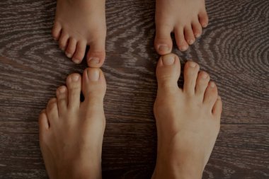 Bir çocuğun ayakları ve evde bir yetişkinin ayakları kahverengi ahşap bir zeminde ayakkabısız, alt manzaralı, ailece