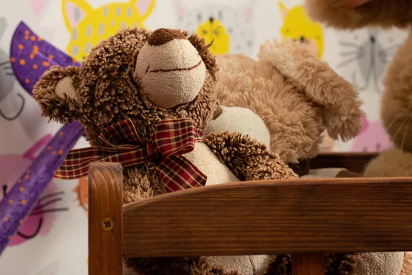 soft brown teddy bear sits in a children\'s wooden bed in a children\'s room on a blurred background