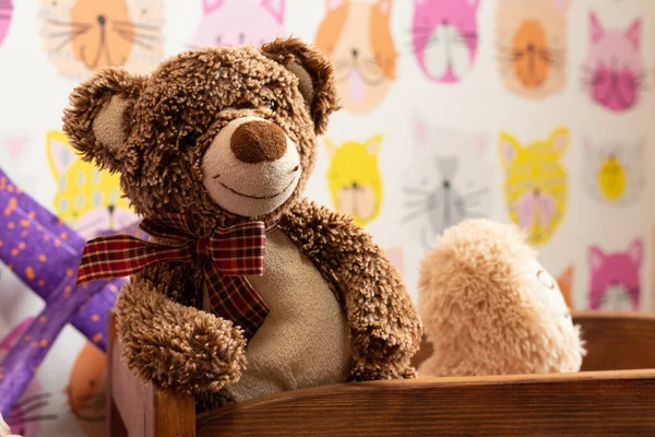 soft brown teddy bear sits in a children\'s wooden bed in a children\'s room on a blurred background