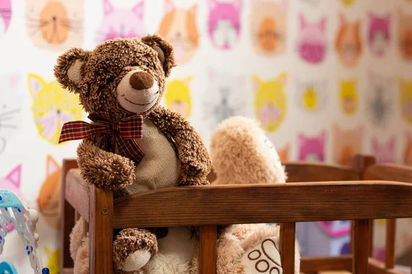 soft brown teddy bear sits in a children\'s wooden bed in a children\'s room on a blurred background