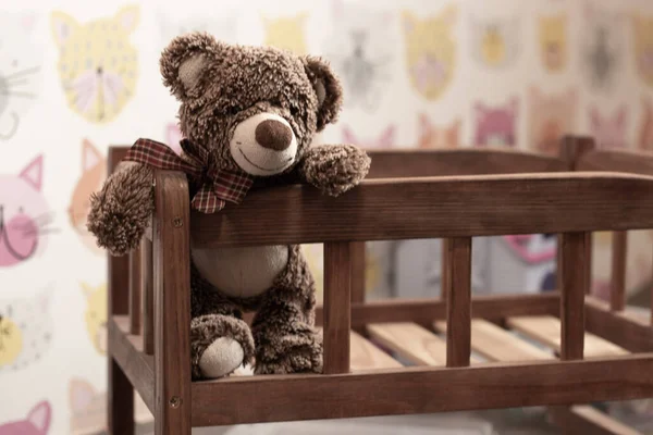 soft brown teddy bear sits in a children\'s wooden bed in a children\'s room on a blurred background