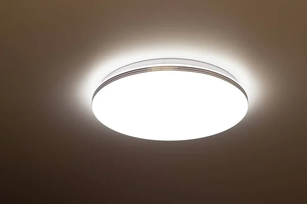 round flat lamp shines on the ceiling in the dark in the room