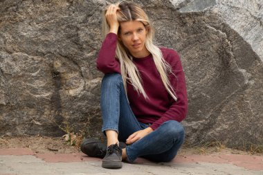 Sonbaharda Ukrayna 'da bir taşın arka planında kırmızı yün kazaklı genç bir kız oturuyor.