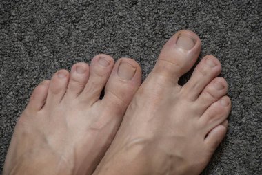 Gri bir ev halısı üzerinde kadın ayakları, ayakkabısız kadın ayakları.